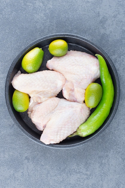 Raw chicken wings and chili pepper on black plate.