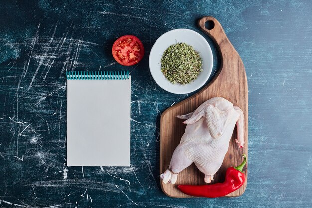 Raw chicken with herbs and spices and a recipe book aside.