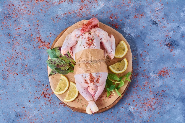 Raw chicken with herbs on a wooden board on blue