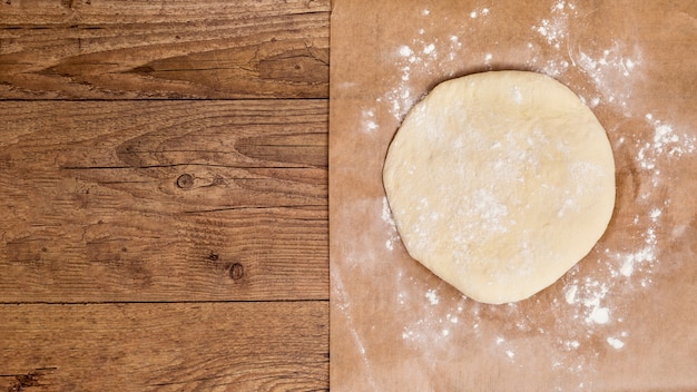 Raw circular flatten dough on parchment paper over the wooden table