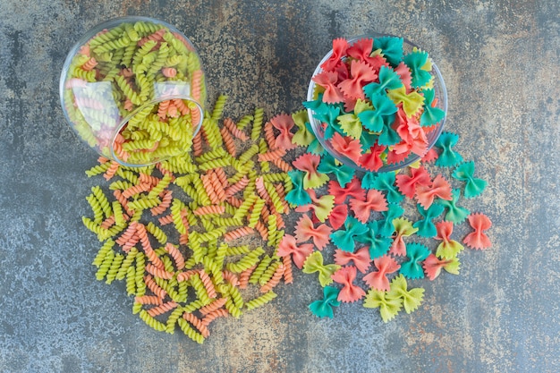 Raw colorful farfalle and fusilli pasta , on the marble surface.