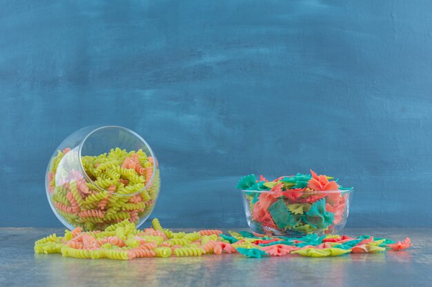 Raw colorful farfalle and fusilli pasta , on the marble surface.