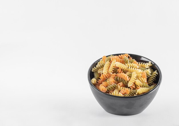 Raw colorful fusilli pasta in dark bowl.