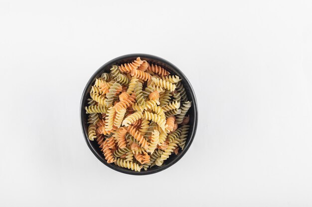 Raw colorful fusilli pasta in dark bowl.