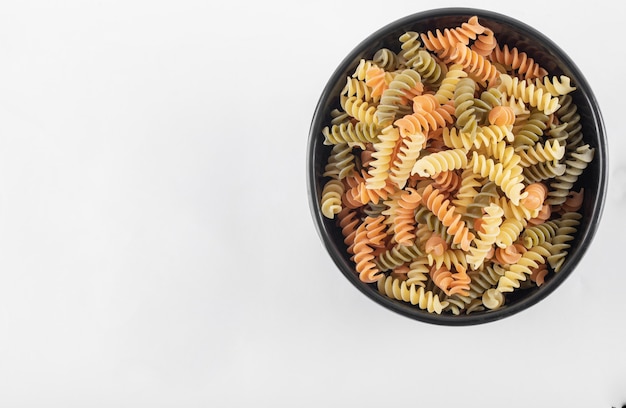 Raw colorful fusilli pasta in dark bowl.