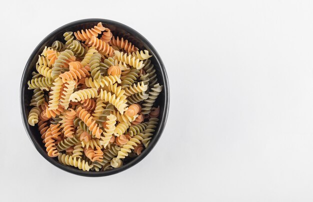 Raw colorful fusilli pasta in dark bowl.