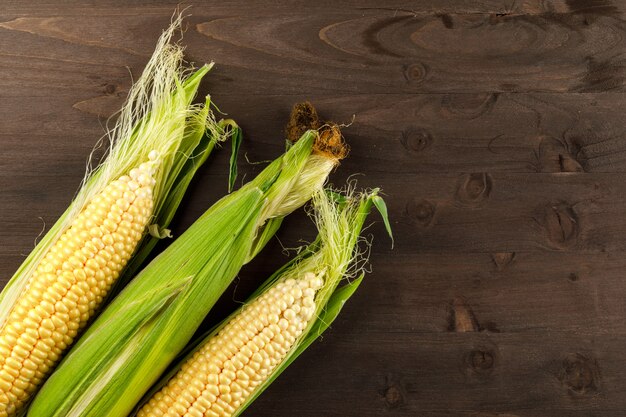 Raw corn cobs on a dark wooden table. top view.