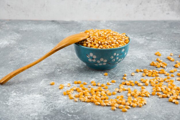 Raw corn kernels in blue bowl with wooden spoon.