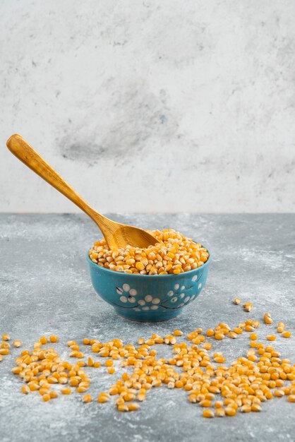 Raw corn kernels in blue bowl with wooden spoon.