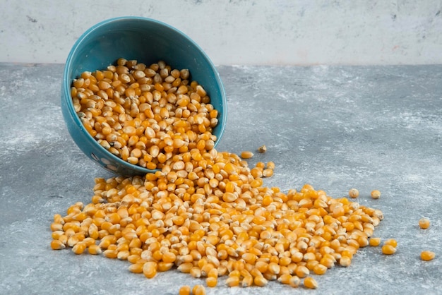 Raw corn kernels out of bowl on marble surface.