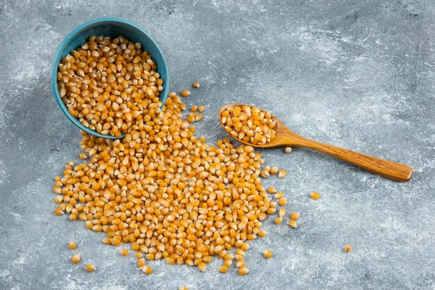 Raw corn kernels out of bowl on marble surface.