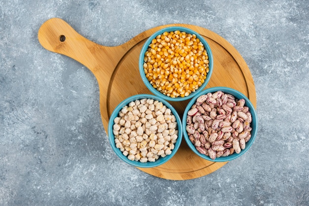 Raw corns, beans and chickpeas in blue bowls.