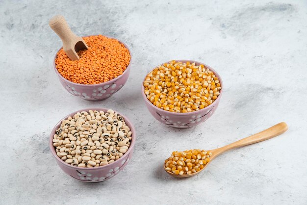 Raw corns, beans and red lentil in purple bowls.