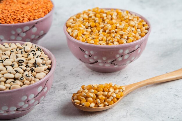 Raw corns, beans and red lentil in purple bowls.
