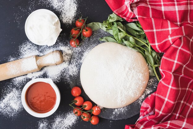 Raw dough for pizza with ingredients on kitchen counter