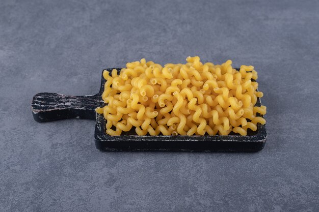 Raw dry macaroni on black wooden board.