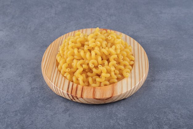 Raw dry macaroni on wooden plate.