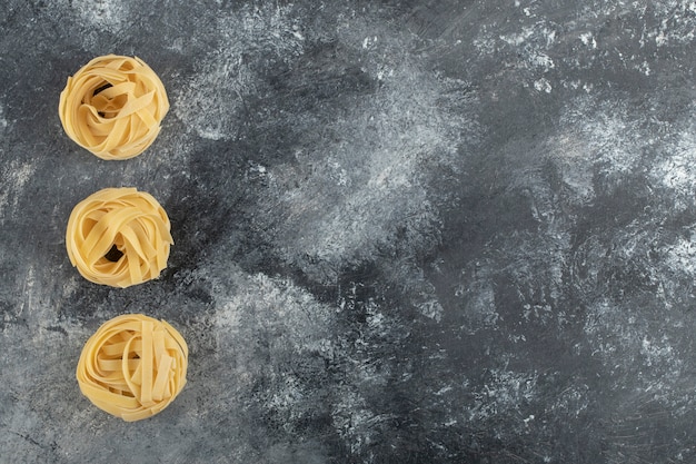 Tagliatelle secche crude del nido su una tavola di marmo.