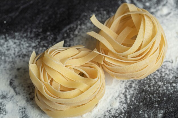 Raw dry nest pasta with flour on black.