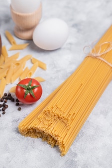 Сырые сухие спагетти, перевязанные коричневым шпагатом, на мраморном фоне. фото высокого качества