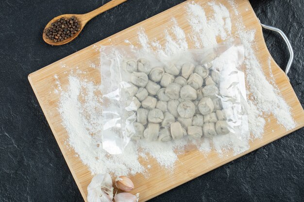 Raw dumplings with flour on wooden board.