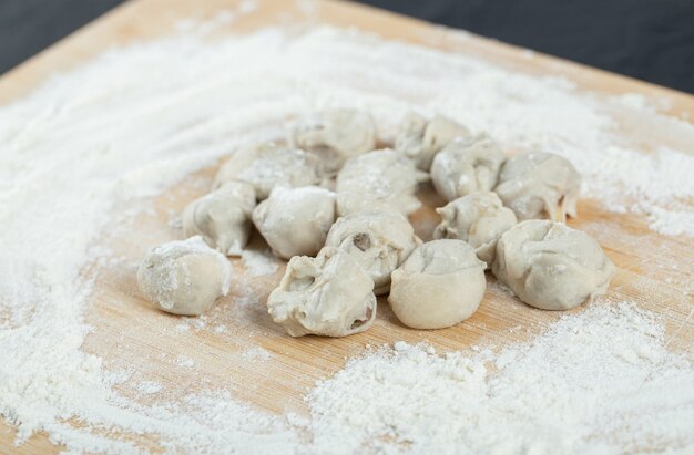 Raw dumplings with flour on wooden board.