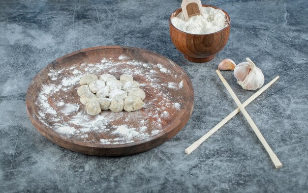 Raw dumplings with flour on wooden board.