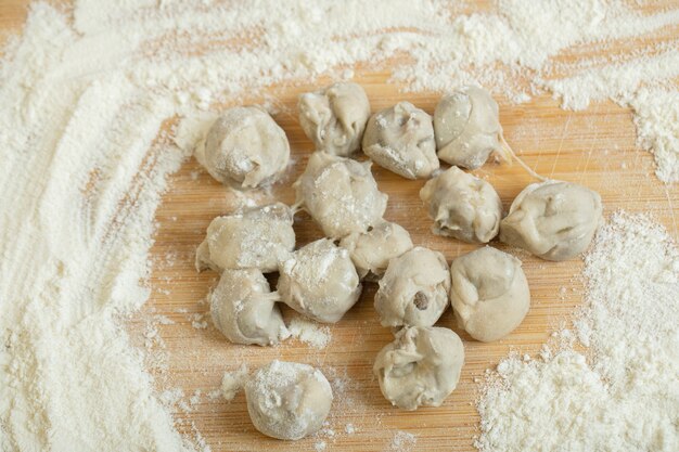 Raw dumplings with flour on a wooden board