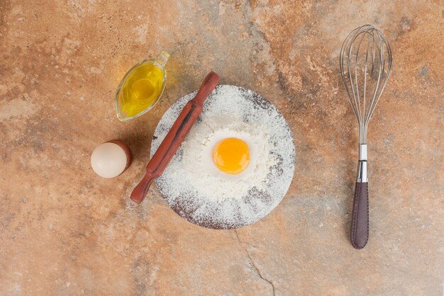 Raw egg with wgisk and wooden board .