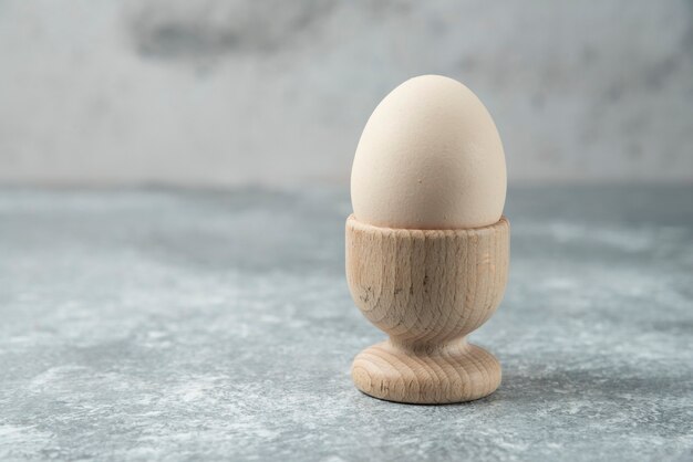 Raw egg in wooden bowl on marble table.