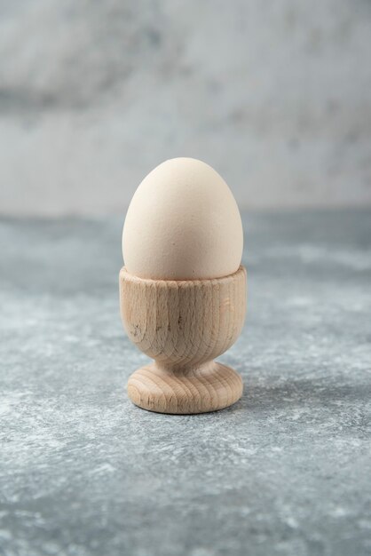 Raw egg in wooden bowl on marble table.