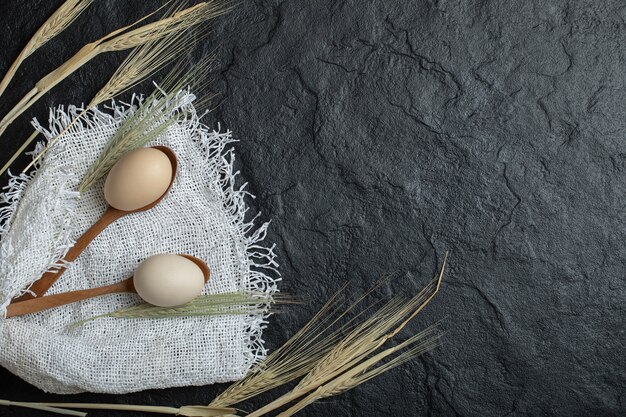 Raw eggs and ears of wheat on dark surface