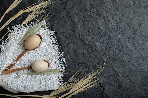 Raw eggs and ears of wheat on dark surface