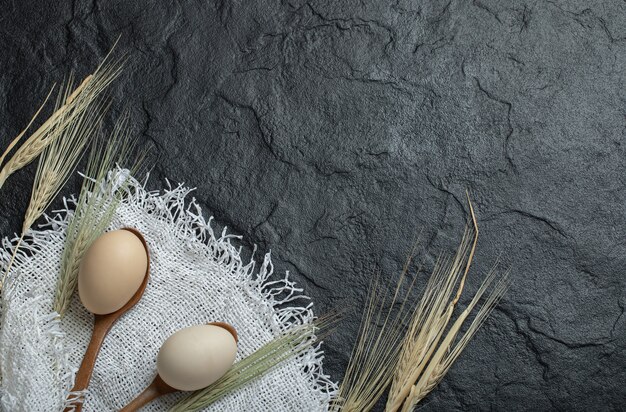 Raw eggs and ears of wheat on dark surface