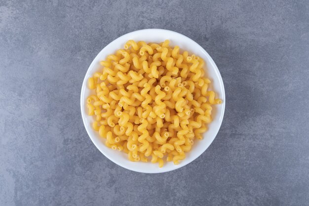 Raw elbow macaroni on white plate.