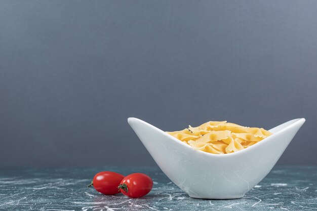 Raw farfalle pasta in white bowl and tomatoes. High quality photo