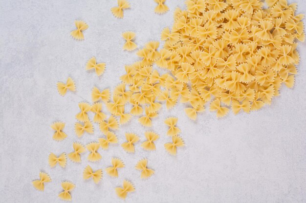 Raw farfalle pasta on white table.