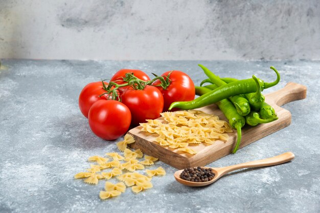 Raw farfalle, tomatoes and chili peppers on wooden board.