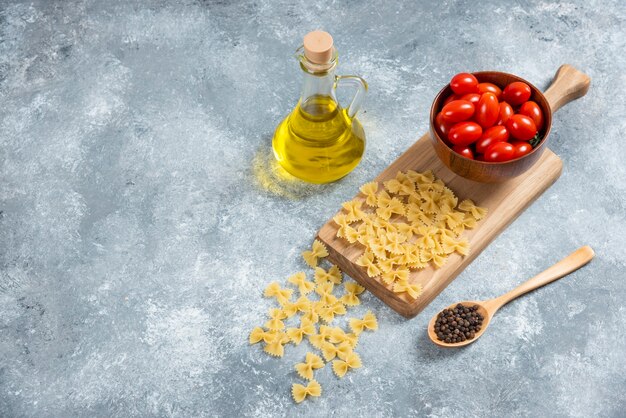 Raw farfalle, tomatoes and olive oil on wooden board.