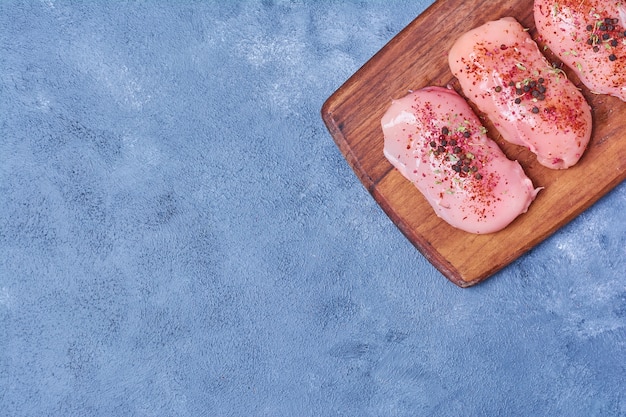 Foto gratuita filetto crudo con spezie su una tavola di legno sull'azzurro