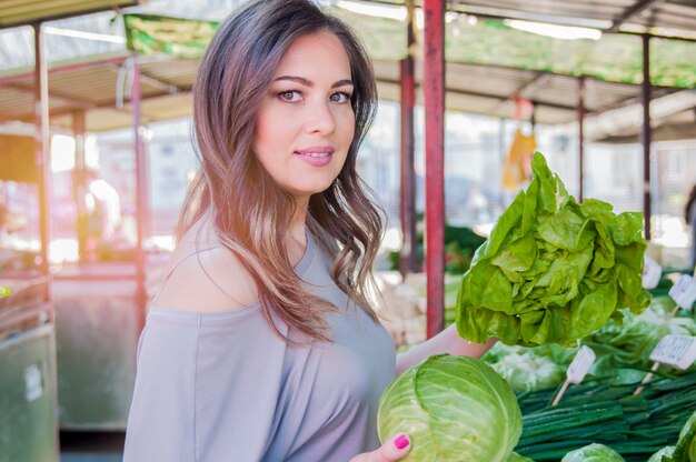 生の食べ物、野菜のコンセプト。彼女の手にキャベツを持っているカジュアルな服の中に笑っている美しい女の子の肖像画。健康な肌、光沢のある茶色の髪。