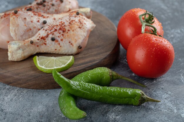 Raw fresh chicken on chopping board with fresh vegetables.