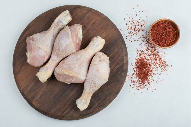 Raw fresh chicken legs with red hot chili peppers on white background.