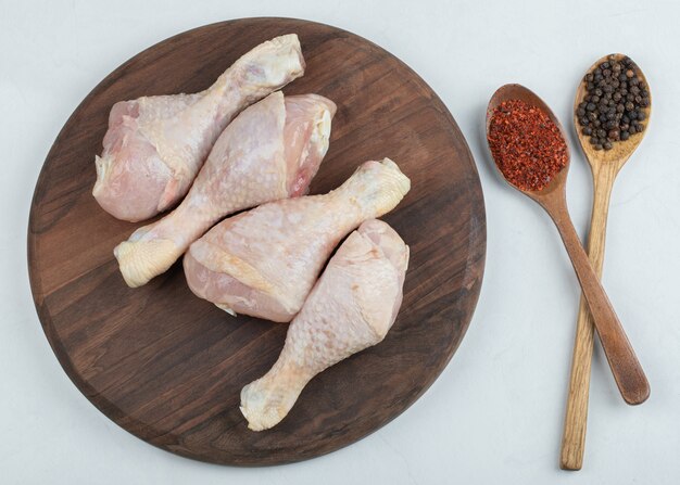 Raw fresh chicken legs with two spoon peppers on white background.