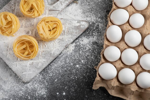 Raw fresh tagliatelle nests with flour on wooden board and eggs