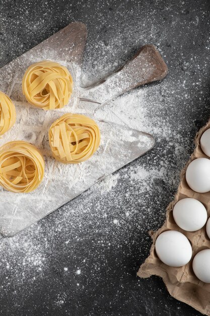 Raw fresh tagliatelle nests with flour on wooden board and eggs