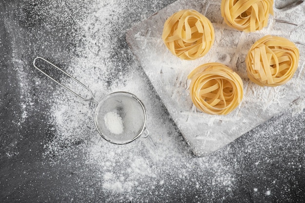 Raw fresh tagliatelle nests with flour on wooden board