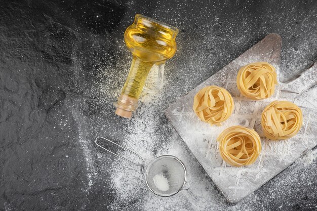 Raw fresh tagliatelle nests with on wooden board with bottle of oil