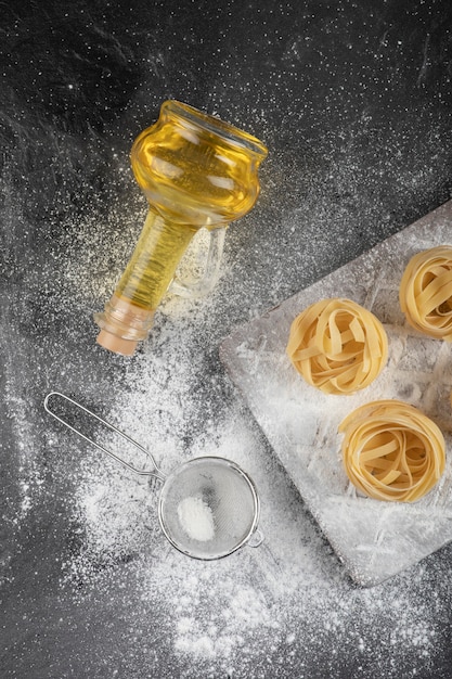 Raw fresh tagliatelle nests with on wooden board with bottle of oil