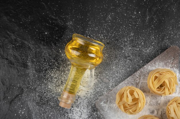 Raw fresh tagliatelle nests with on wooden board with bottle of oil